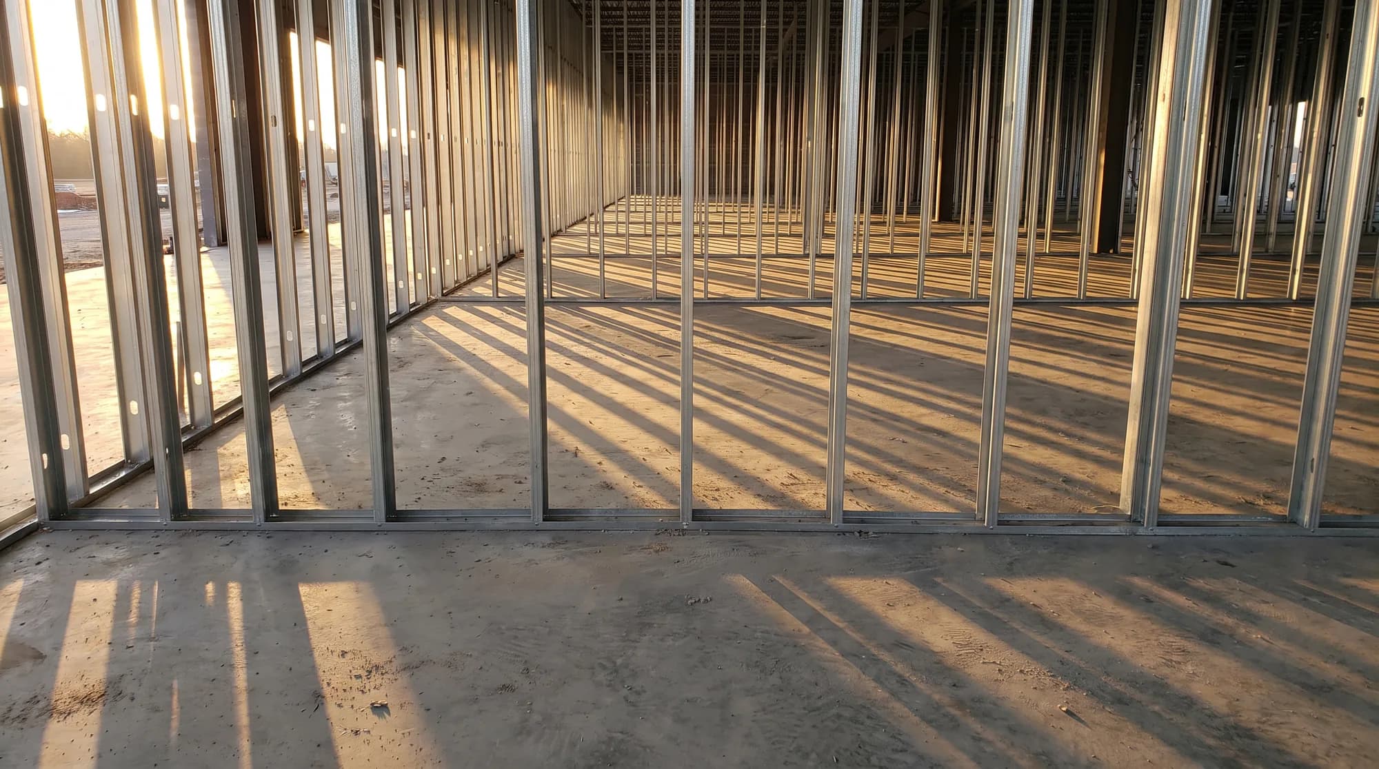 A repeating grid of galvanized steel studs across an open floor plate, long shadows between them